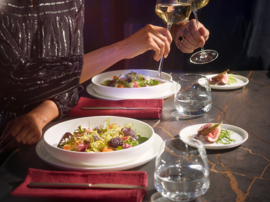 Elegante Dinner-Szene mit Bone China Porzellan von Rosenthal: Feine wei&szlig;e Teller, stilvoll angerichtete Speisen und edle Gl&auml;ser schaffen eine luxuri&ouml;se Atmosph&auml;re.