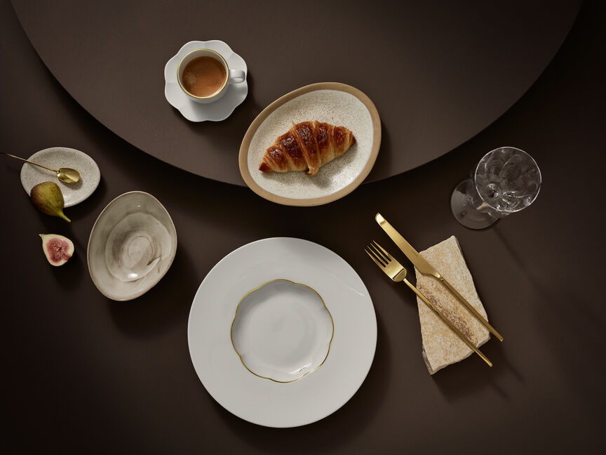 Servizio di piatti in gres di Rosenthal Sonetto: tavola apparecchiata con piatto, tazza, croissant, posate e coppetta da dessert nei caldi toni del marrone e del crema.