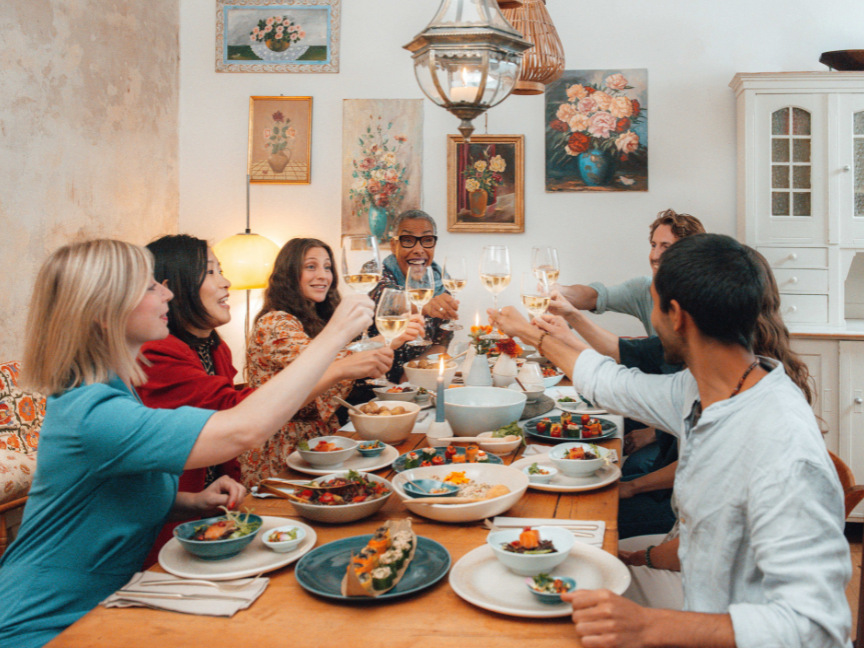 A cheerful group of friends raising their wine glasses in a toast at a lavishly laid dining table.