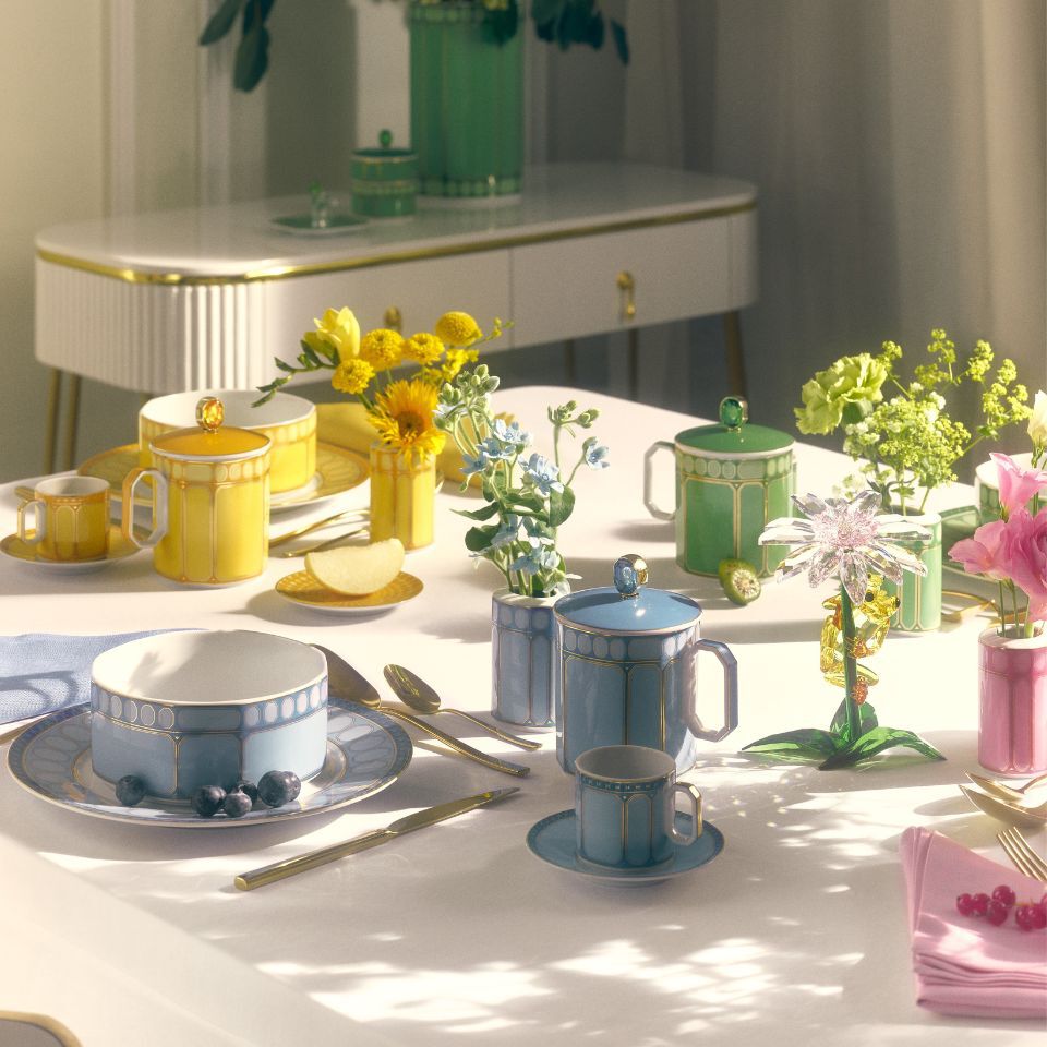 Bright and elegant Signum tableware by Swarovski x Rosenthal in vibrant pastel tones of yellow, blue, green, and pink, featuring geometric patterns and gold detailing, beautifully styled with fresh flowers and modern cutlery on a sunlit table.
