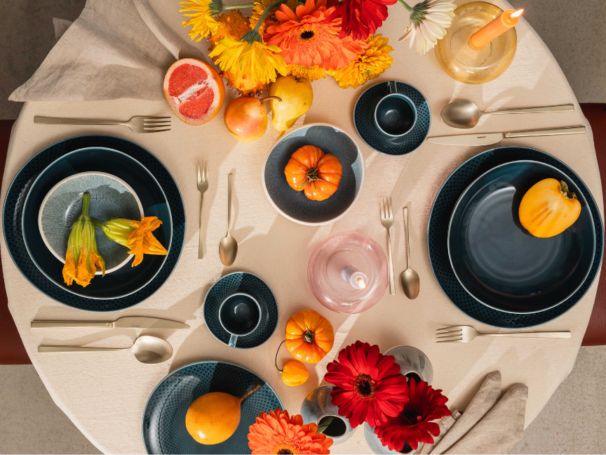 A round table set from above with dark blue tableware by Rosenthal, gold cutlery, orange gerberas and pumpkins.