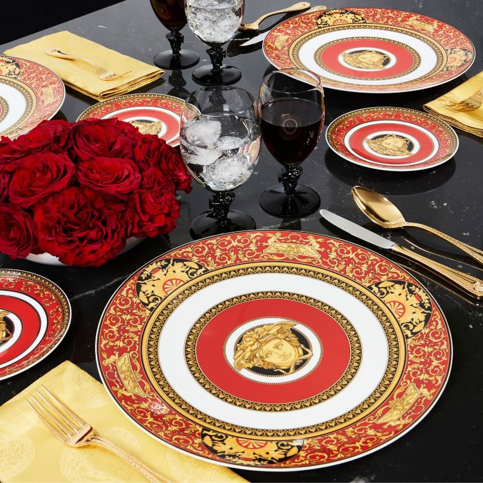 Striking Versace Medusa Red porcelain set with red, gold, and black plate design centered around the Medusa head, styled with gold cutlery and red roses on a black table.