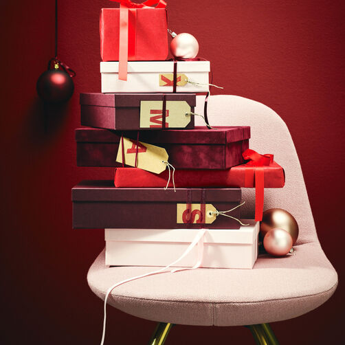 Unterschiedlich gro&szlig;e Geschenkschachteln in verschiedenen Rott&ouml;nen auf rosa Stuhl gestapelt