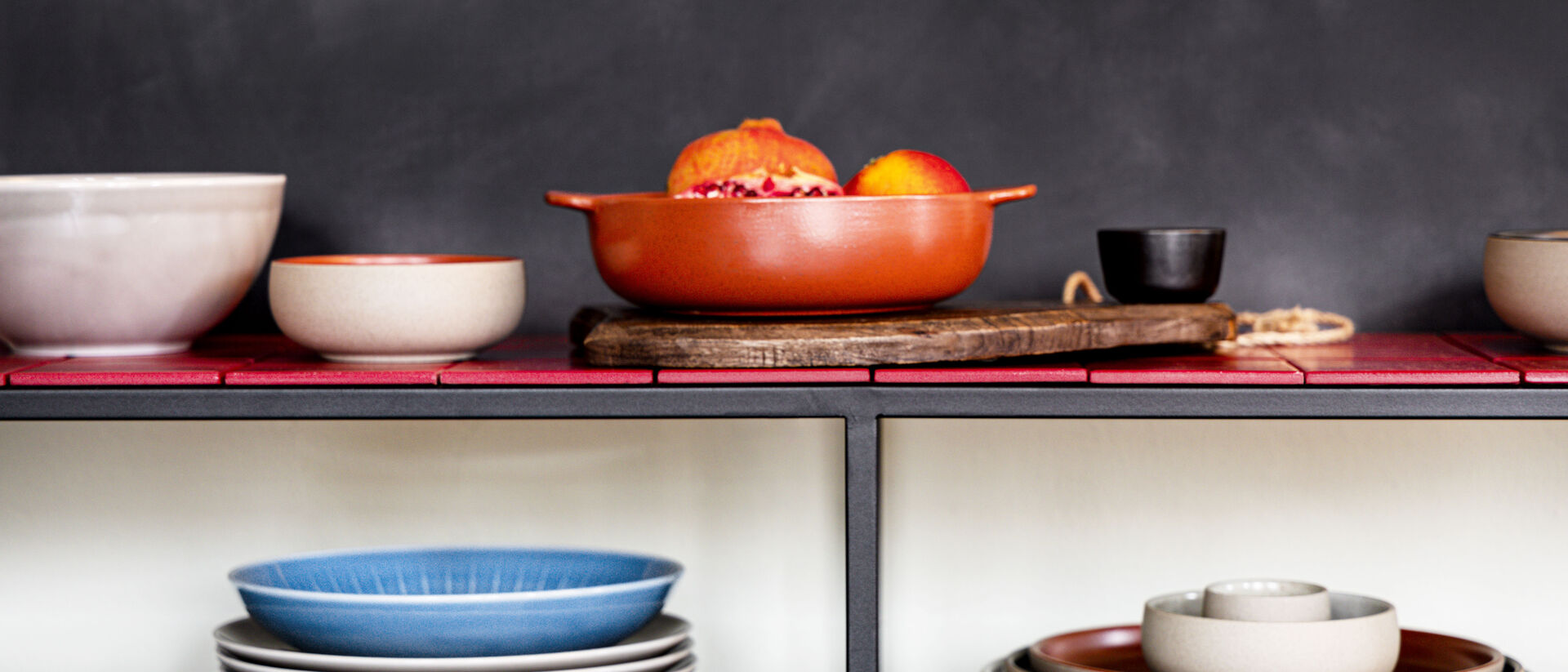 Servizio di piatti in gres di Rosenthal su scaffale aperto: piatti e ciotole nei toni del blu, crema e terracotta, disposti in modo decorativo con una fruttiera.