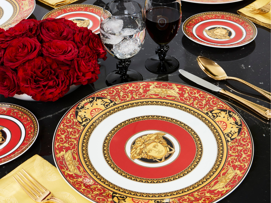 A lavishly laid table featuring intricately decorated Rosenthal tableware in red and gold, complemented by red roses, elegant glasses and gold cutlery.
