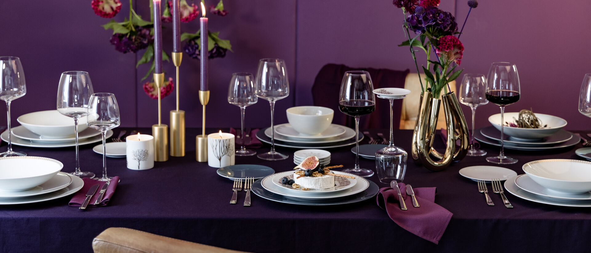 Festlich gedeckter Weihnachtstisch mit elegantem Porzellan, goldenen Kerzenhaltern, Weingläsern und violetten Akzenten.