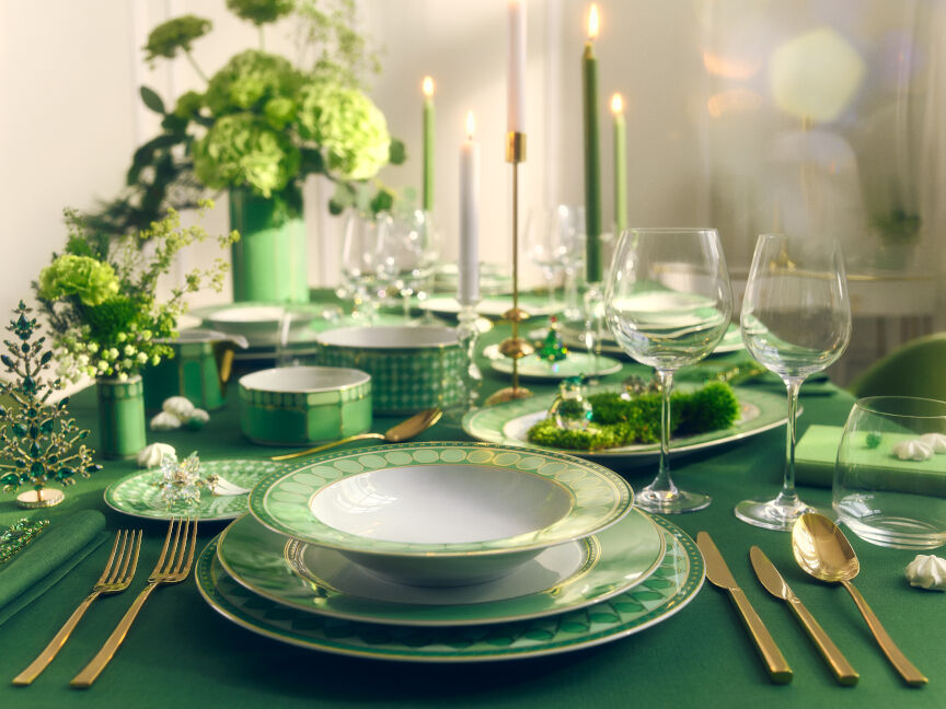 Eleganter, festlich gedeckter Tisch in Grüntönen mit edlem Porzellan, Goldbesteck und floralen Dekoelementen.