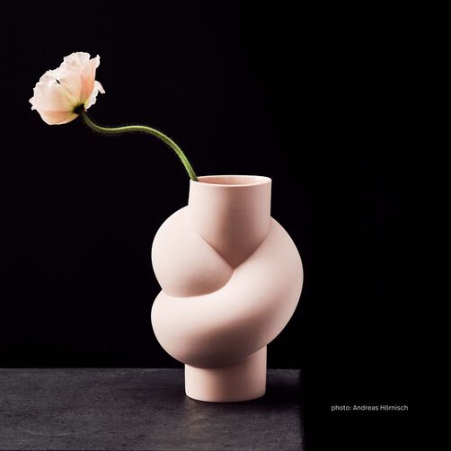 Node Cameo vase with a single salmon coloured flower standing on a dark grey concrete background against a black background.