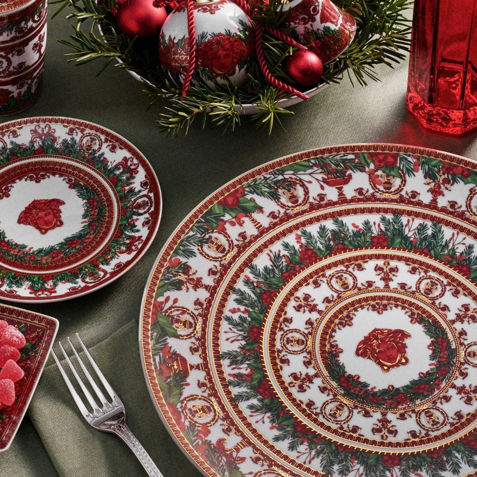Festive Versace I Love Baroque Holiday tableware in red, white, and gold featuring holly and wreath motifs with Medusa accents, styled with Christmas ornaments and greenery.