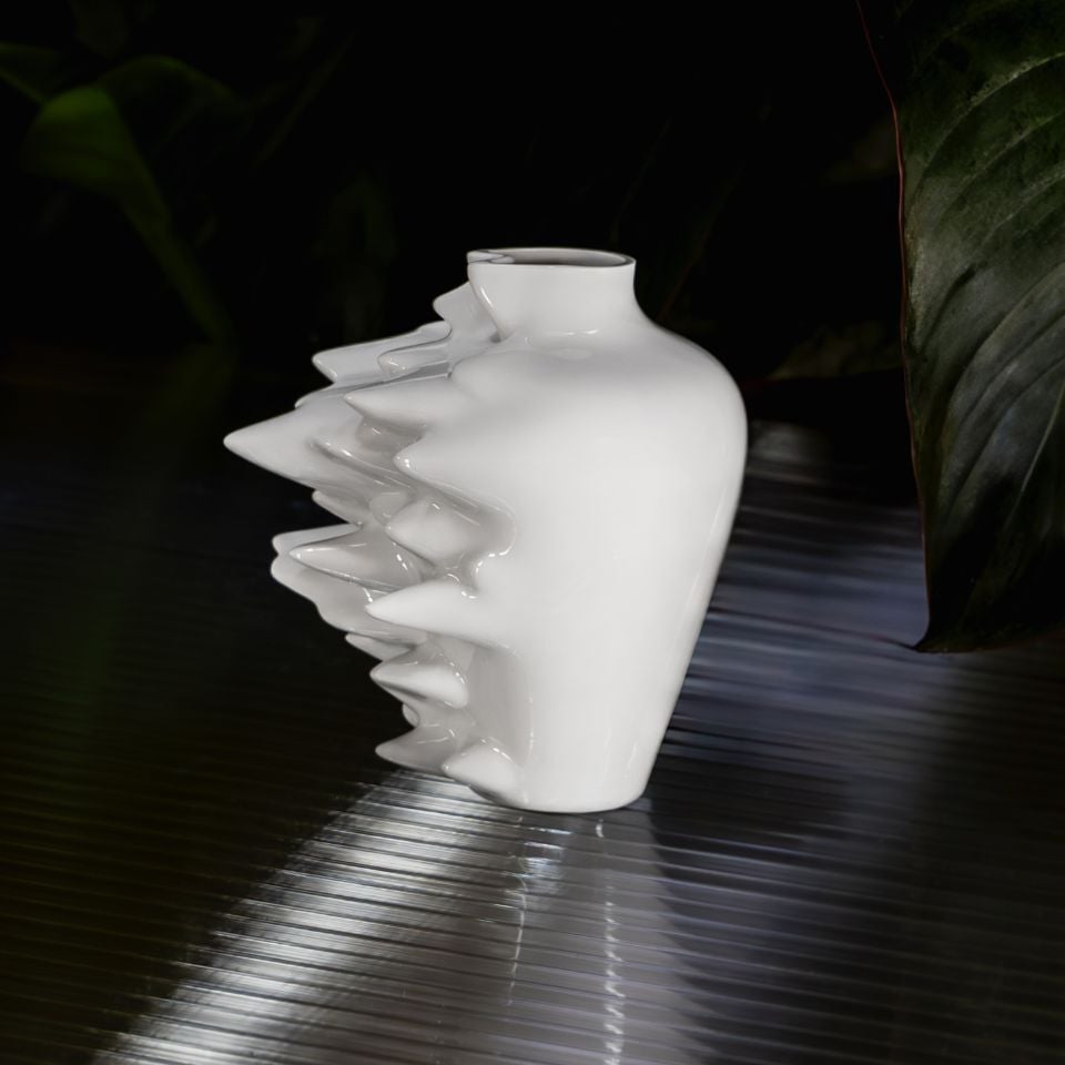 A glossy white vase with bold, angular spikes on one side, standing on a reflective surface.