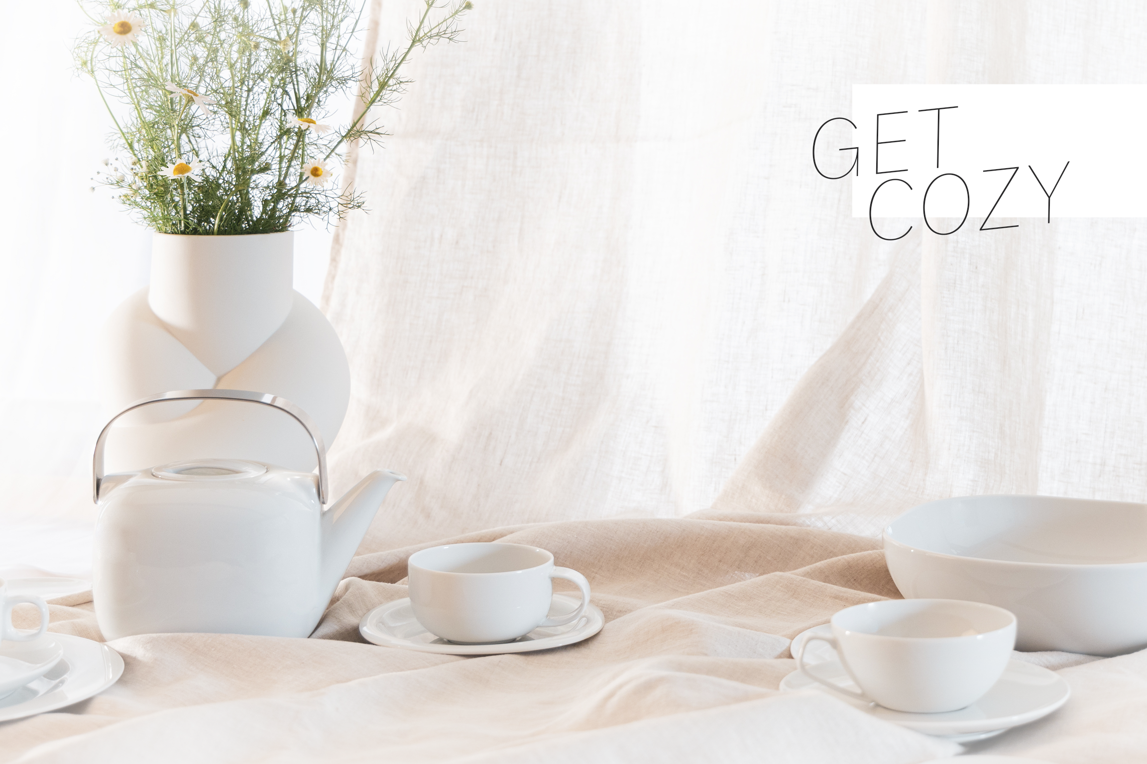 Get cozy with Rosenthal classics White Rosenthal classics Moon, Suomi and TAC are placed in a jumble on a linen blanket, with a white Node vase with flowers in the background and the words GET COZY in the top right-hand corner.