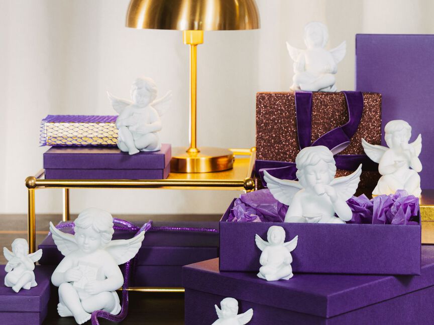 Weiße Porzellanengel auf violetten Geschenkboxen in festlicher Tischdekoration.