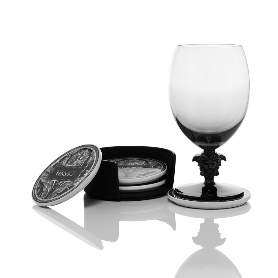 Versace black-stemmed goblet on top of a porcelain coaster with a baroque pattern and logo, next to a velvet box containing additional matching coasters.