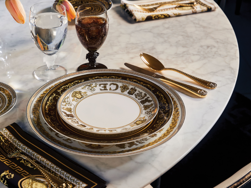 Versace Medusa von Rosenthal Speiseteller in Wei&szlig;, Schwarz und Gold mit ornamentalem M&auml;ander- und Barockrand sowie zentralem Medusa-Motiv, gedeckt auf hellem Marmortisch mit goldfarbenem Besteck und Glas.