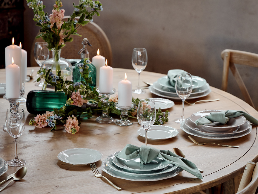 Romantisch gedeckter Holztisch mit Rosenthal Maria Porzellan, salbeigrünen Stoffservietten, goldfarbenem Besteck, weißen Stumpenkerzen und Blumenarrangement in Vintage-Vasen