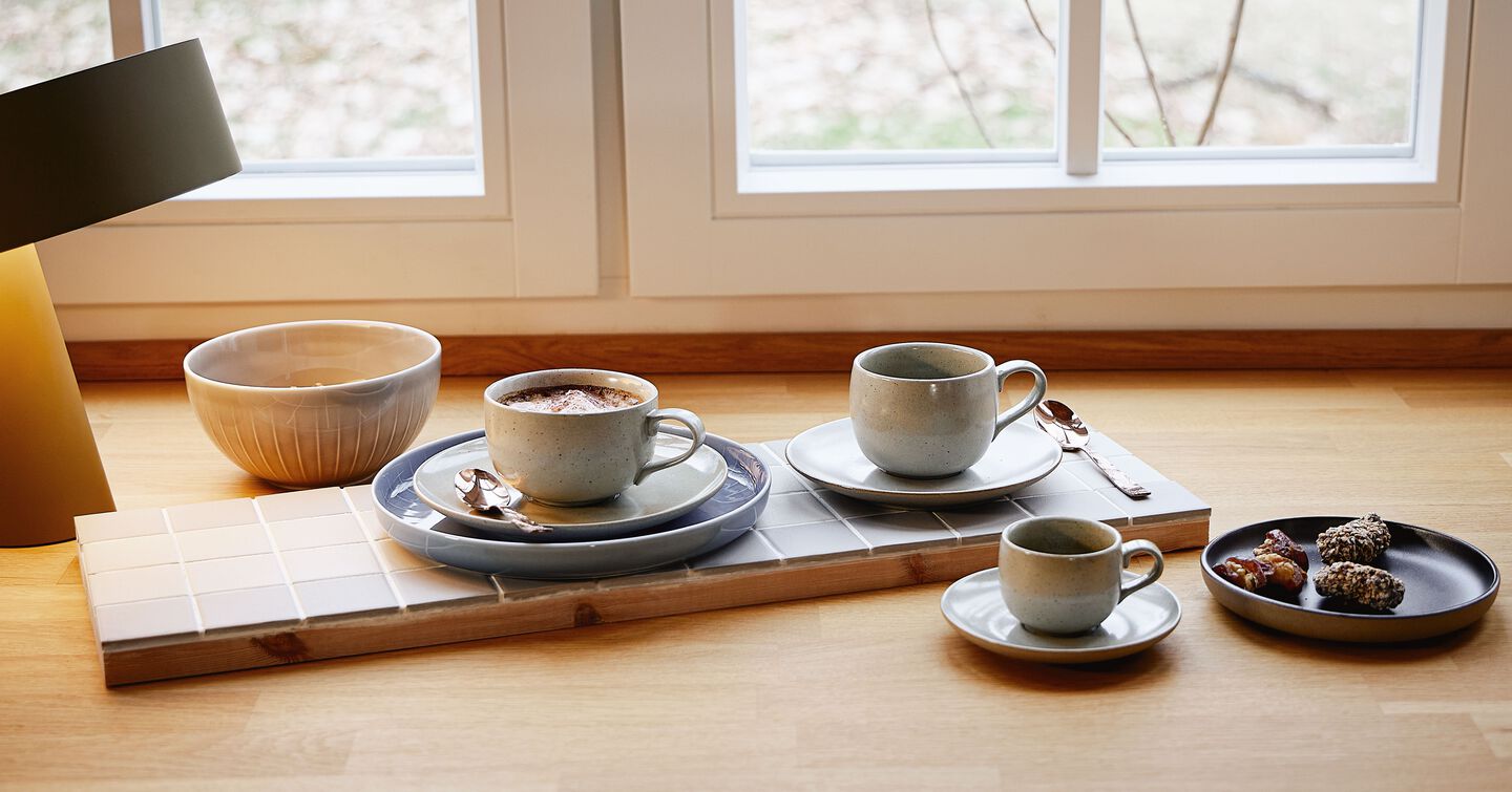 Tasses &agrave; caf&eacute; de diff&eacute;rentes formes de Rosenthal, dont des tasses bomb&eacute;es et cylindriques avec soucoupes, dispos&eacute;es sur un plateau en bois avec une surface carrel&eacute;e dans un environnement de cuisine lumineux.