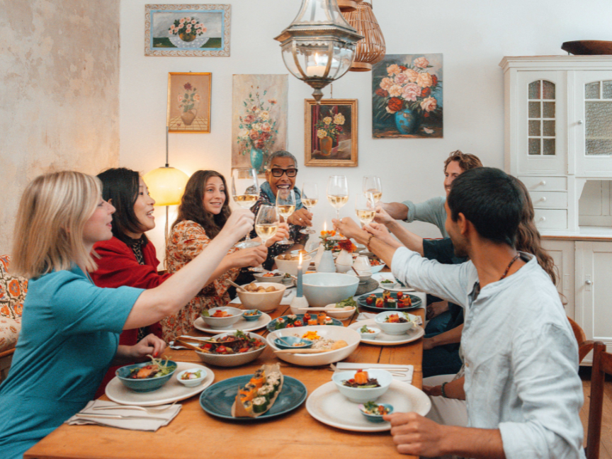 A convivial dinner gathering around a festively laid table featuring Rosenthal&rsquo;s antipasti tableware. Several people raise their glasses together as starters are served on colourful ceramic plates and bowls.