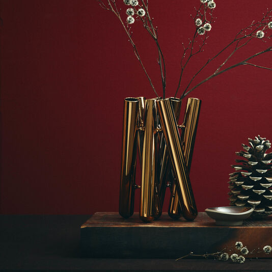 Seven Gold Vase mit einzelnen Weidenk&auml;tzchen gef&uuml;llt steht auf einem Holzbrett vor bordeaux-farbigem Hintergrund