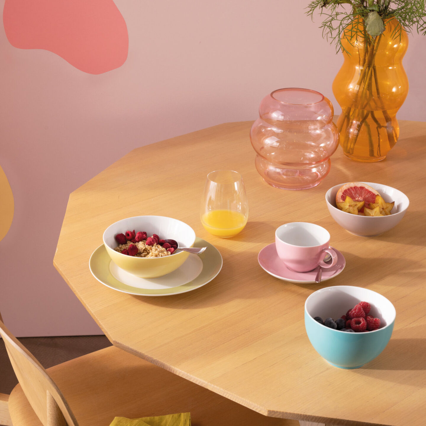 Thomas Sunny Day yellow cereal bowl filled with cereals on a yellow plate, empty light pink coffee cup and light blue cereal bowl with fruits on wooden table
