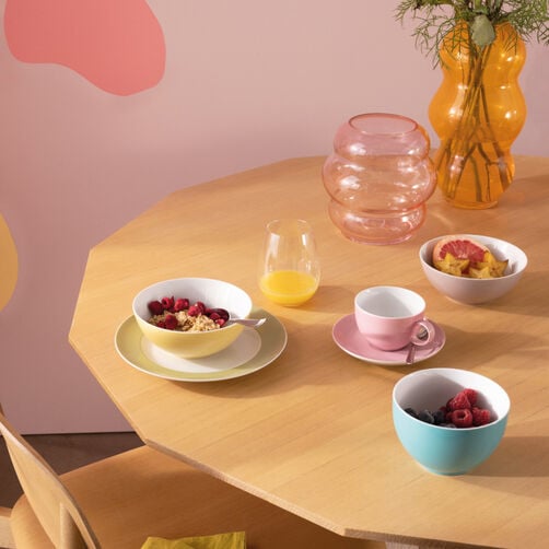 Thomas Sunny Day Thomas Sunny Day yellow cereal bowl filled with cereals on a yellow plate, empty light pink coffee cup and light blue cereal bowl with fruits on wooden table