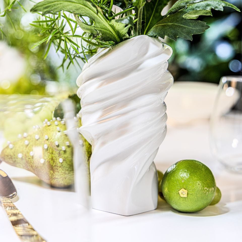 A twisted white vase filled with greenery, surrounded by limes and a textured table setting.