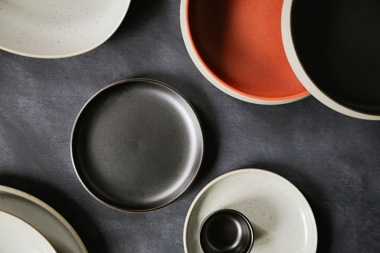 Modern Rosenthal porcelain plates in organic shapes and natural shades such as black, cream and terracotta, arranged against a dark background.