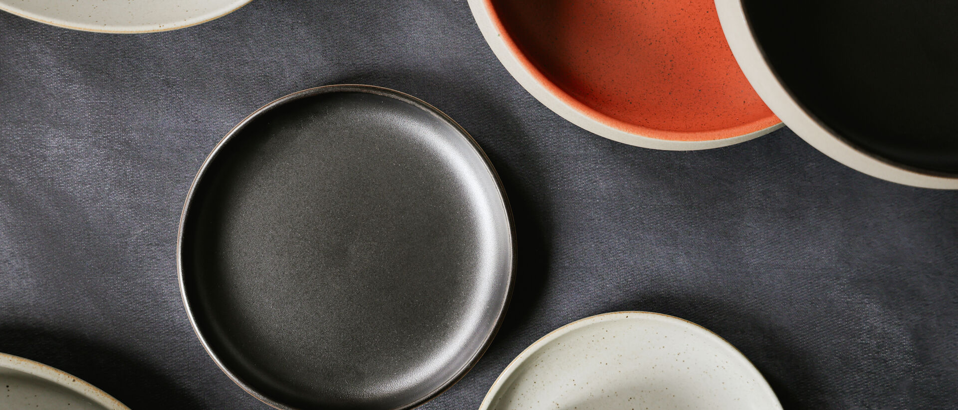 Moderne Rosenthal Teller aus Porzellan in organischen Formen und nat&uuml;rlichen Farbt&ouml;nen wie Schwarz, Creme und Terrakotta, arrangiert auf dunklem Hintergrund.