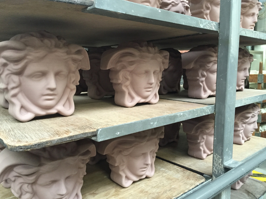 Ungebrannte, rosafarbene &bdquo;Versace Medusa&ldquo;-Skulpturenk&ouml;pfe werden vor dem Brennen auf Holzregalen in einer Werkstatt gelagert.