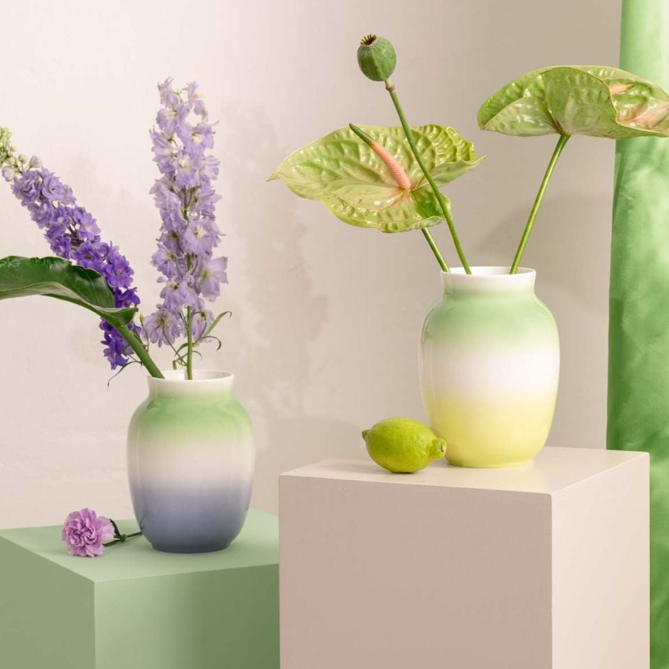 Two soft gradient vases in green and lavender tones with fresh flowers and a lime, arranged on pastel-colored cubes.