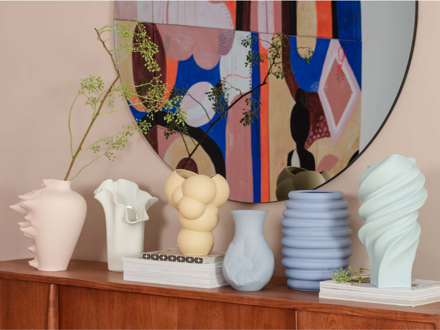 Modern designer vases by Rosenthal arranged on a sideboard, complemented by an ornate mirror and delicate flowers.