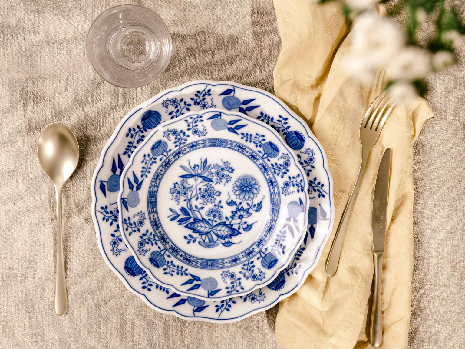 Zwei Hutschenreuther Blau Zwiebelmuster Teller aufeinander gestellt, links ein Suppenlöffel, rechts Gabel und Messer auf einer Leinenserviette und Leinen-Tischdecke, alles von oben fotografiert