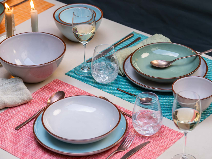 A modern dining table set with Rosenthal tableware in soft pastel shades. Colourful plates, bowls and cups are arranged on coloured placemats, complemented by wine glasses, cutlery and candles to create a stylish, contemporary table setting.