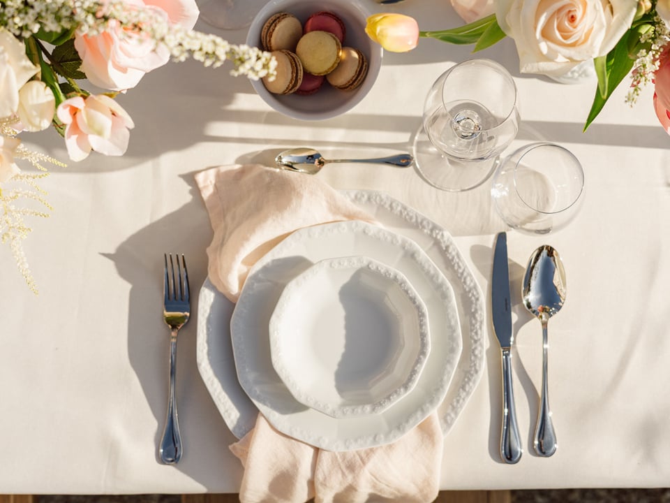 Set table with different plates, cutlery und glasses. Dekoration with flowers and a bowl with macarons