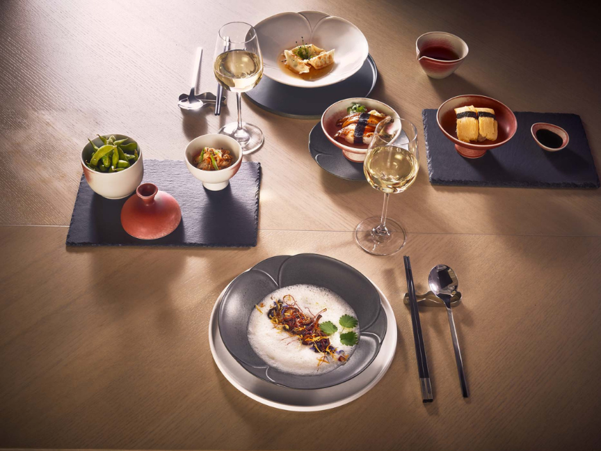 Elegantly set table with Asian-inspired dishes served on Rosenthal Bloom porcelain with blossom-shaped plates, accompanied by white wine and chopsticks