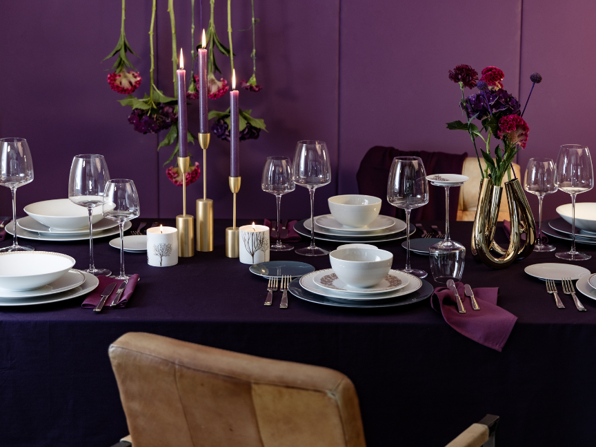 Elegant evening table setting with white Rosenthal tableware, golden accents, purple tablecloth, wine and water glasses, floral decorations, and candles