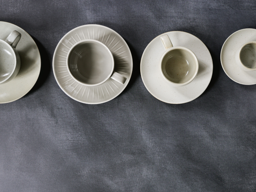Diverses tasses &agrave; caf&eacute; et mugs Rosenthal aux formes claires et classiques, avec leurs soucoupes assorties, dispos&eacute;s sur un fond gris, de proportions vari&eacute;es, de cylindriques &agrave; l&eacute;g&egrave;rement coniques.