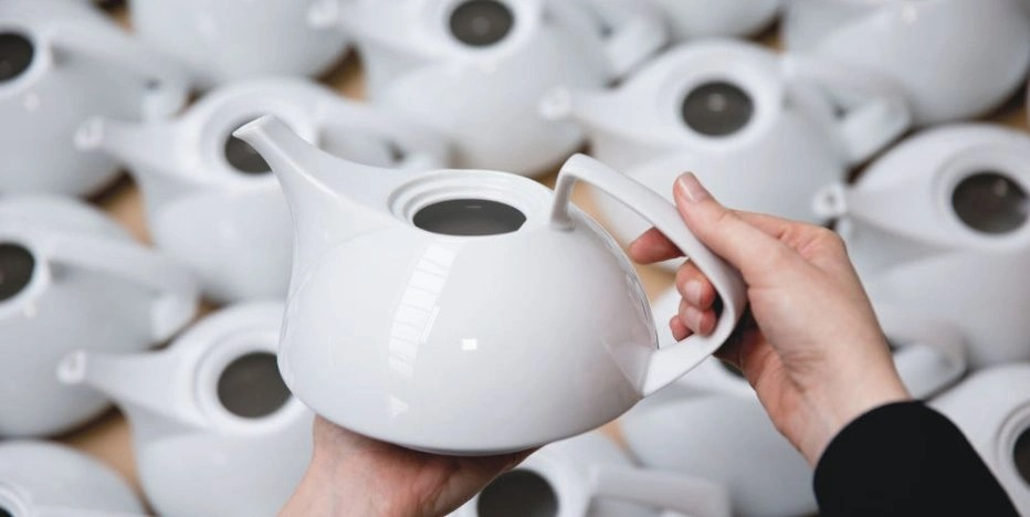 A white TAC teapot is taken out of a mass of many teapots and into focus
