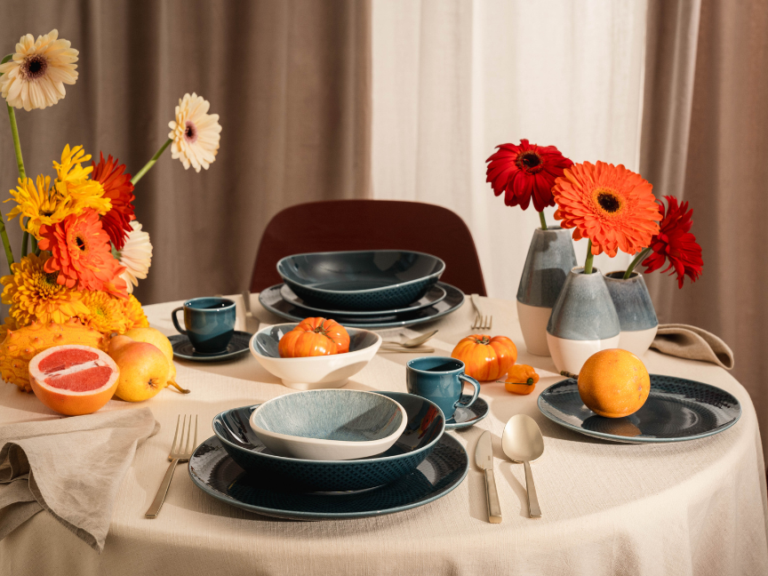 Festive table setting with blue dinnerware, colorful gerbera flowers, pumpkins and fresh fruits