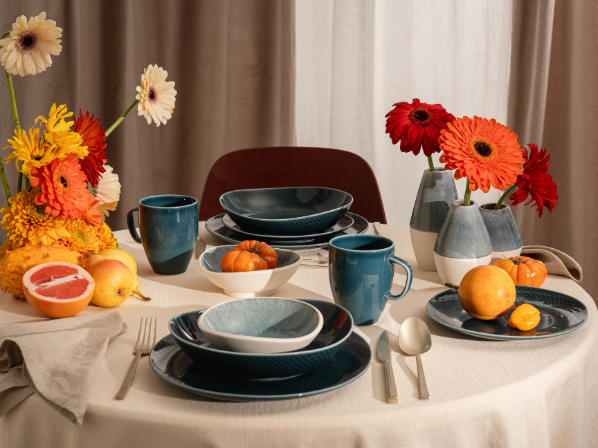 A stylishly laid table featuring Rosenthal tableware in deep shades of blue and grey. Plates, bowls and cups are arranged harmoniously and are accompanied by fresh citrus fruits and colourful flowers.