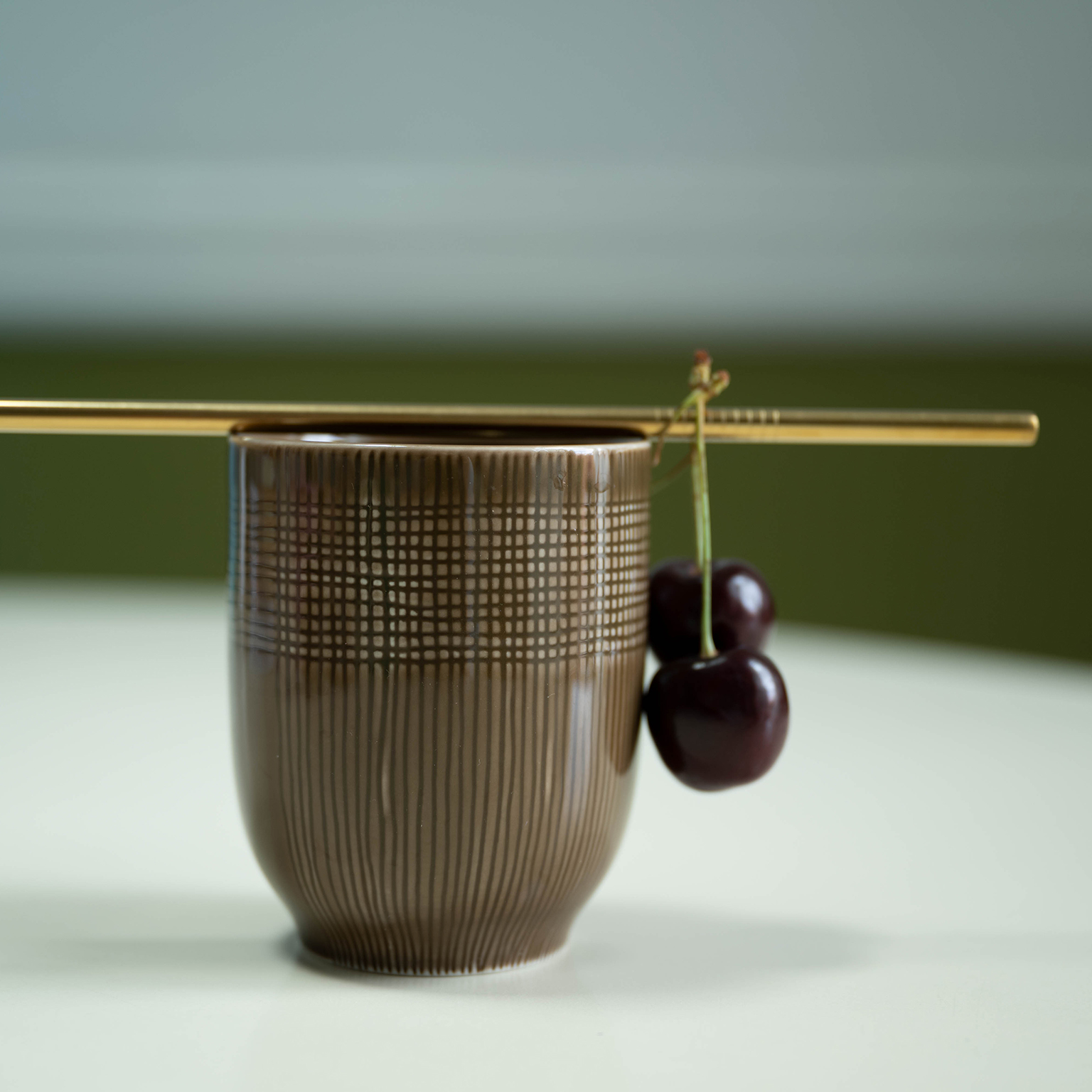A straw with cherries lies on a MUCA cup in the colour Wood.