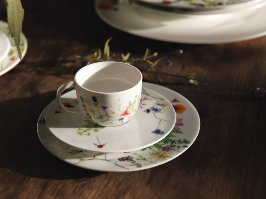Tasse &agrave; caf&eacute; Rosenthal de forme classique et &eacute;l&eacute;gante, avec un bord fin l&eacute;g&egrave;rement &eacute;vas&eacute; et une anse d&eacute;licate, d&eacute;cor floral sur la tasse et la soucoupe, dispos&eacute;e sur une table en bois fonc&eacute;.