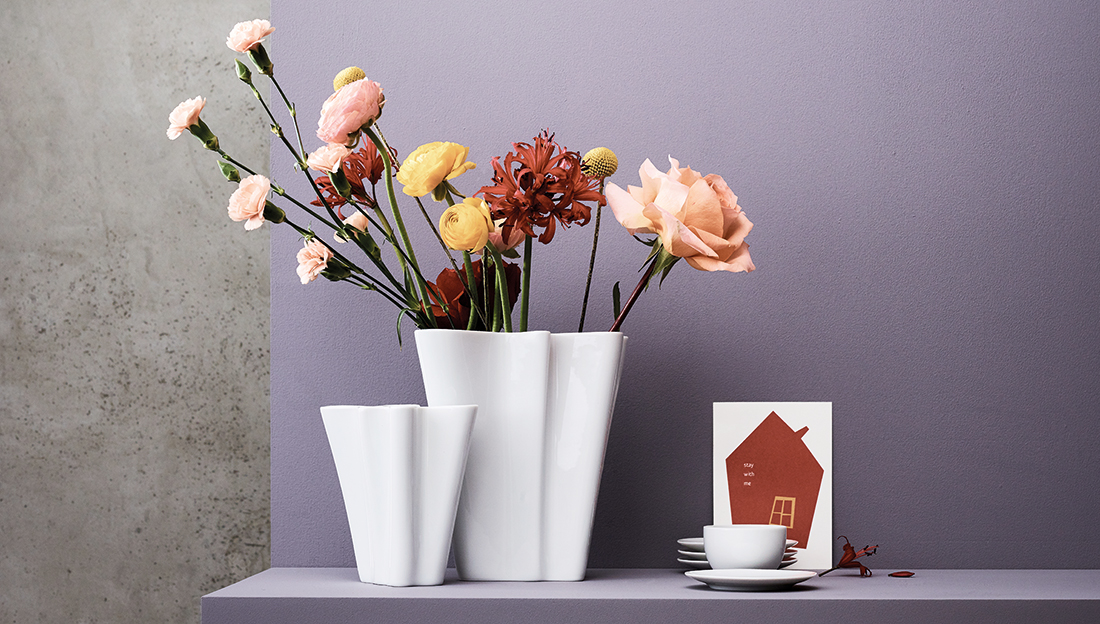 Weiße Rosenthal Flux Porzellanvasen mit Blumenarragnements vor violettem Hintergrund