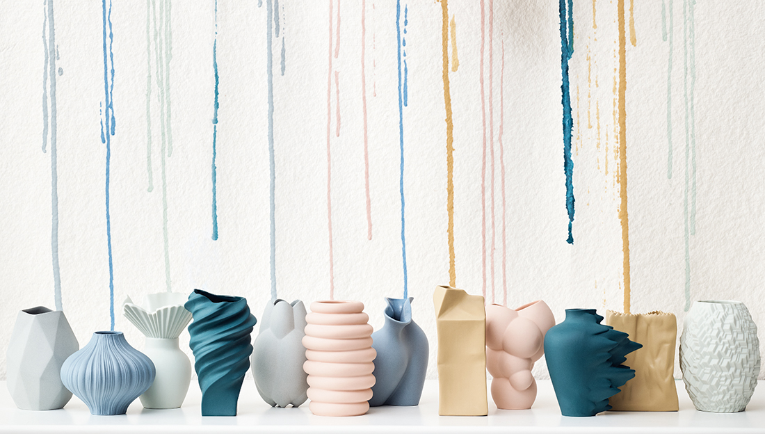 Miniaturvasen in unterschiedlichen Farben vor weißem Hintergrund mit Farbklecksen